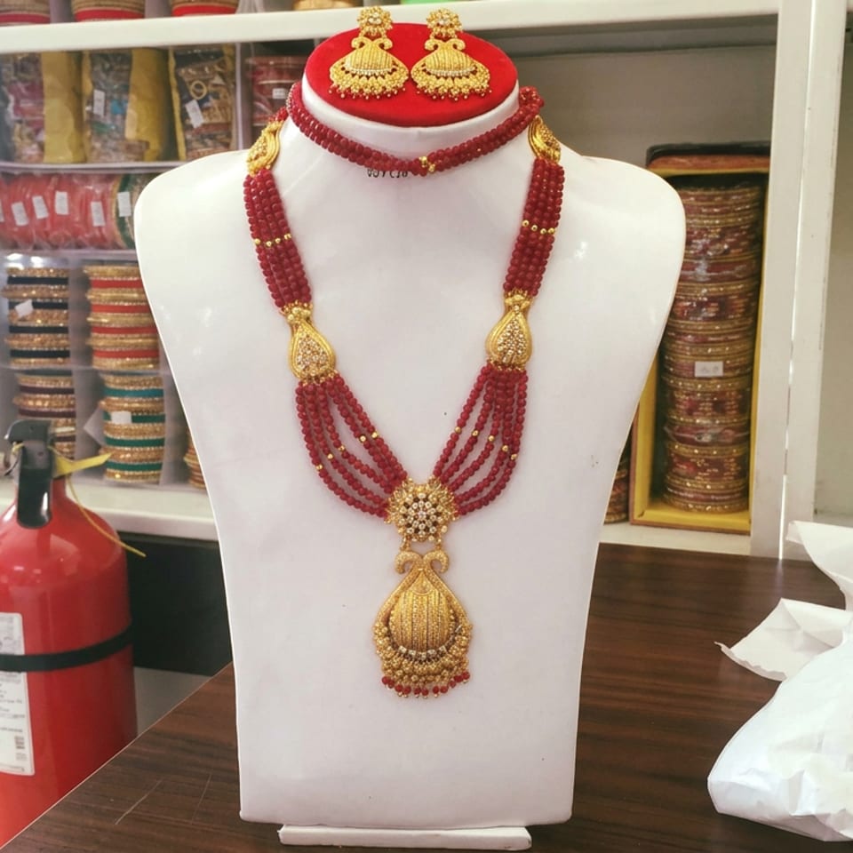 White jewelry display bust showcasing an ornate red and gold necklace set with matching earrings in a shop.